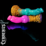 Cerberus-HellHound-Fantasy-Silikondildos in Heroic- und Legendary-Farben auf schwarzem reflektierendem Hintergrund