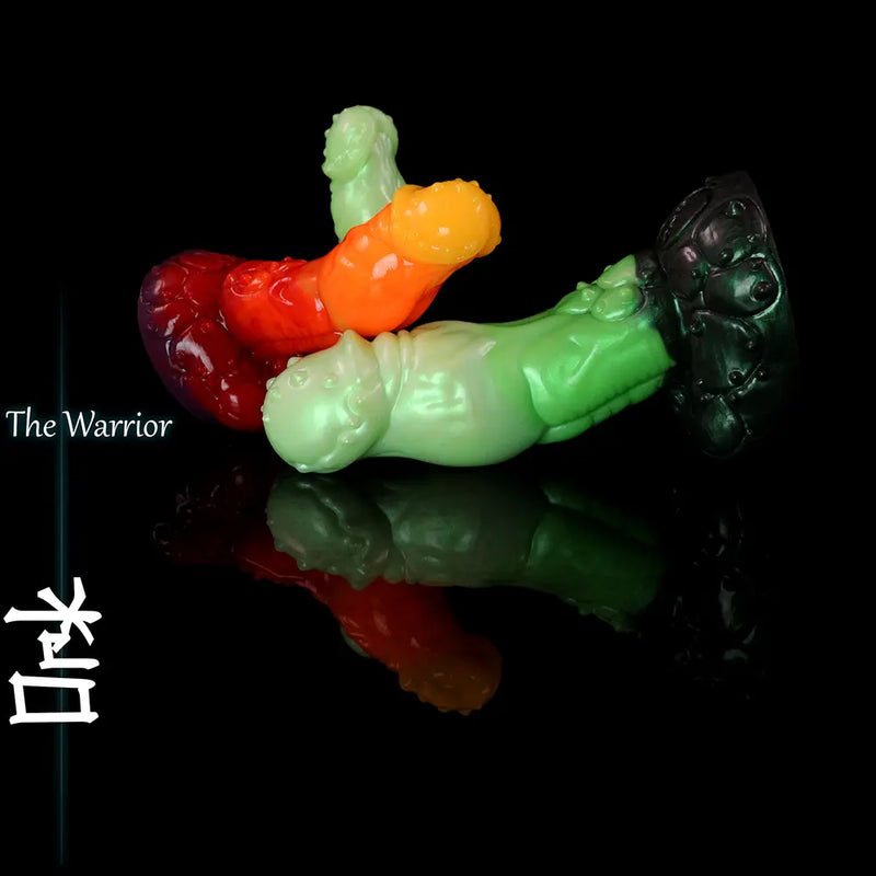 Mehrere grüne, rote und orangefarbene, ork-inspirierte Fantasy-Silikondildos mit modellierter Kreaturenstruktur und breitem Sockel auf schwarzer reflektierender Oberfläche.