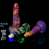 Mehrere Troll-Fantasy-Silikondildos in leuchtenden Marmorfarbmischungen auf einer schwarzen reflektierenden Oberfläche, mit strukturiertem Schuppenschaft und breitem modelliertem Sockel.